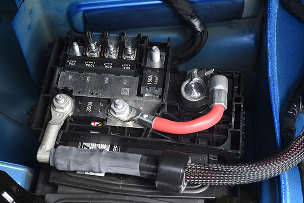 This is the Cadillac battery fuse block. To remove it, you disconnect the short cable from the battery positive post, release the two latches, then fold it back over the adjacent trunk floor. Image: Author.